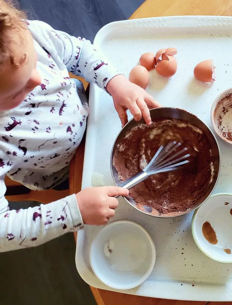 Toddler mixing coconut flour brownies ingredients in a bowl.