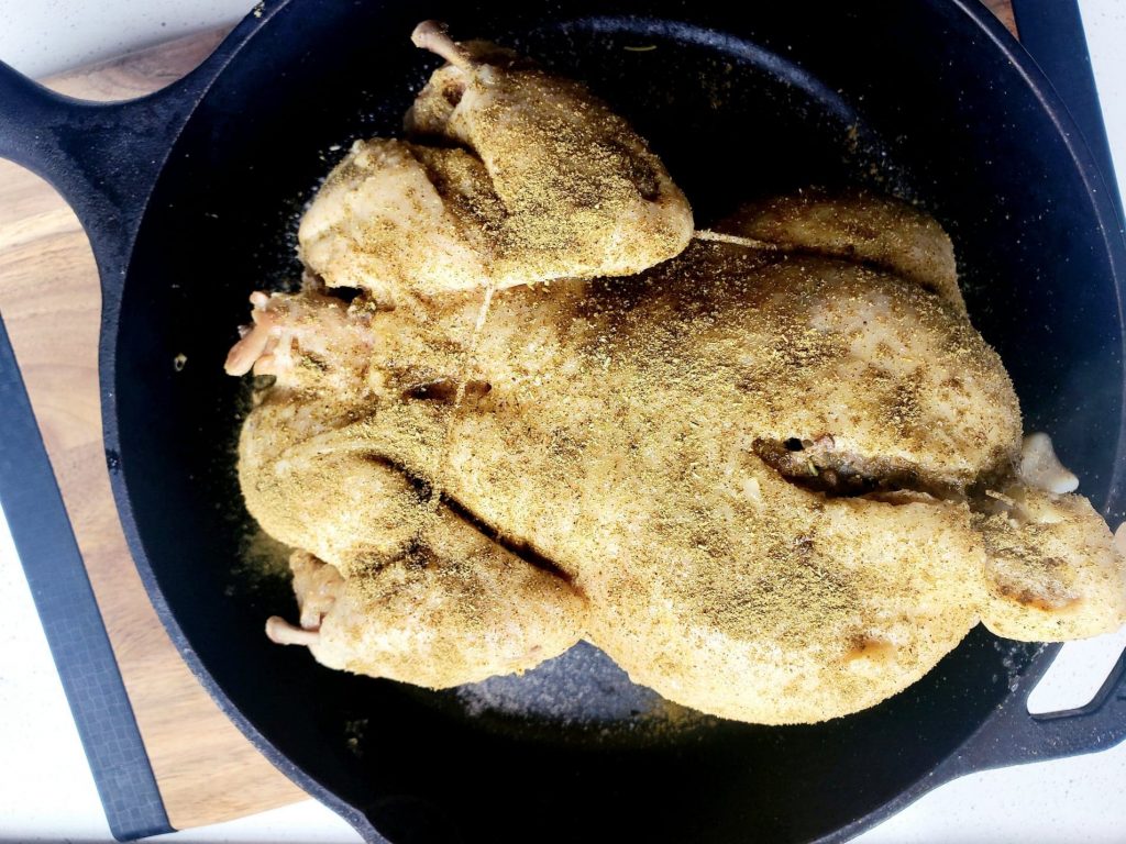Whole chicken seasoned with salt, sage, and rosemary in a cast iron skillet
