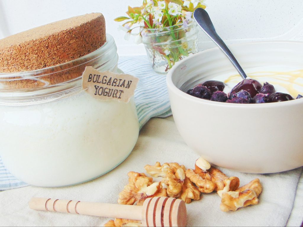 Instant Pot Bulgarian Yogurt in a glass container, yogurt in a bowl with berries and honey, nuts, on a beige and blue background