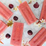 6 cherry yogurt popsicles laying on ice, decorated with cherries and white flowers