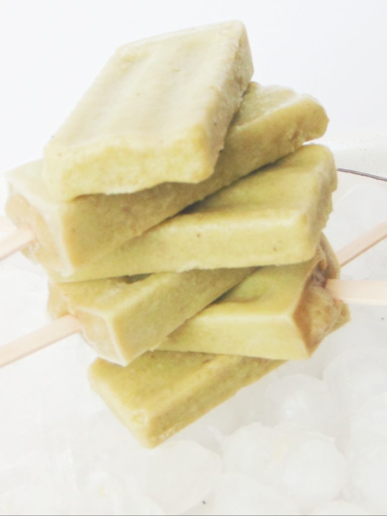 6 creamy banana and avocado popsicles stacked laying on ice