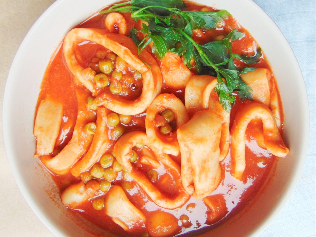 Top view of Instant Pot squid stew with tomato sauce, peas and parsley in white bowl