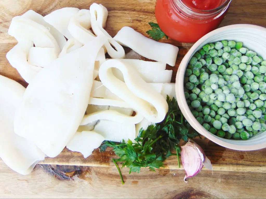 Squid tubes, peas, garlic, tomato sauce and parsley on wooden cutting board used to make Instant Pot squid stew