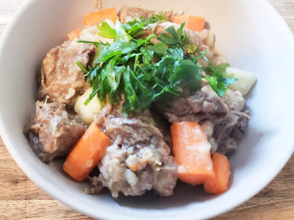 Beef tongue stew with carrots, potatoes and parsley in grey bowl
