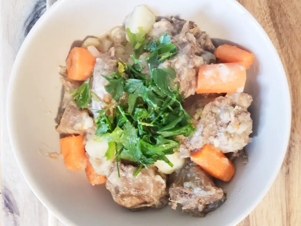 Beef tongue, potatoes and carrots stew garnished with parsley in a white bowl