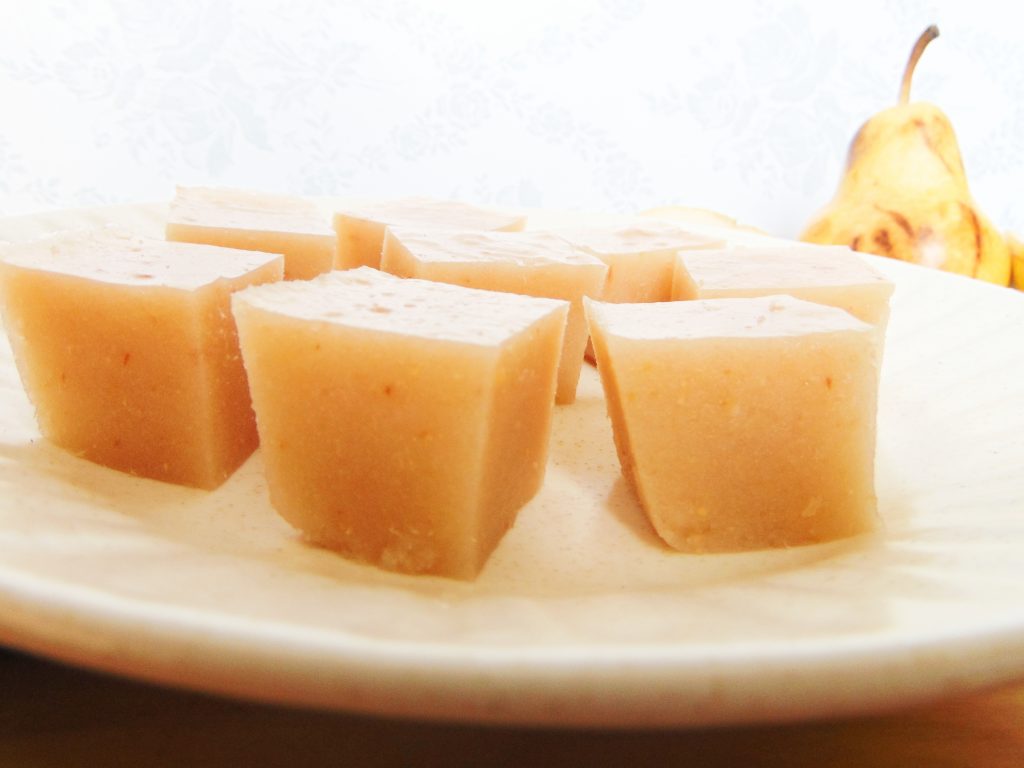 Pear and ginger gelatin cubes on white plate and pear in background