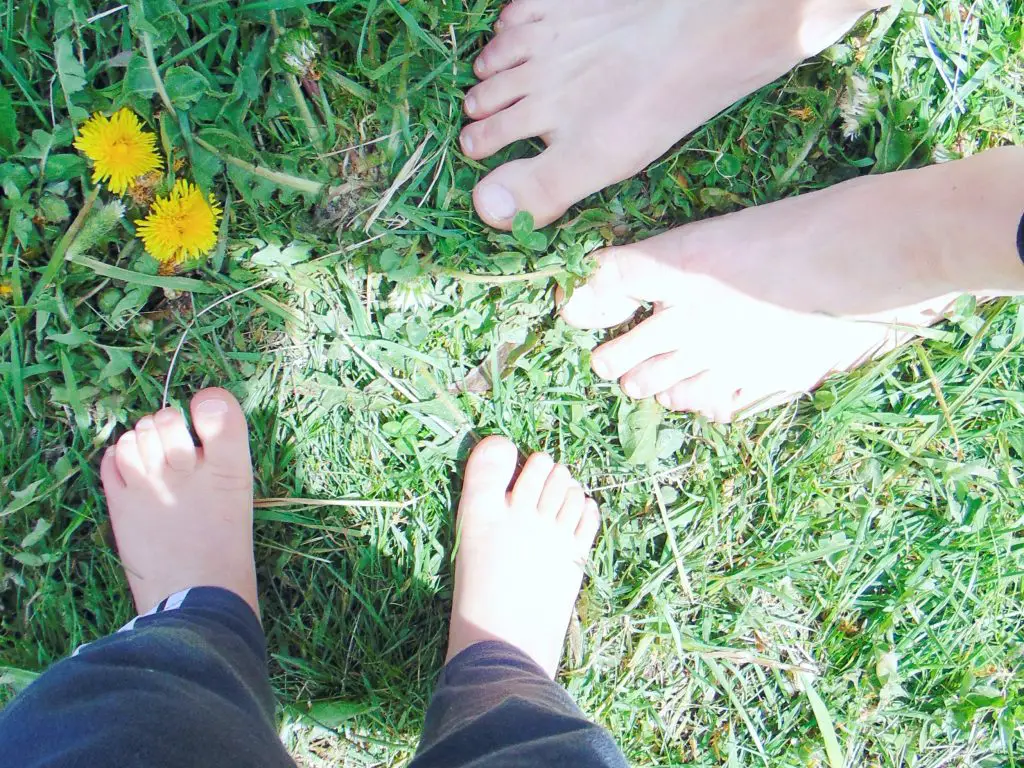 Toddler's and woman's bare feet in the grass showing how spending time outdoors has health benefits