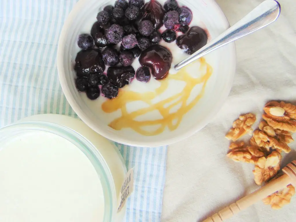 Bowl of Instant Pot Bulgarian yogurt with honey and berries, nuts and more yogurt on beige and light blue background
