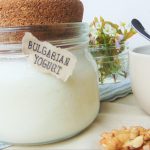 Bulgarian yogurt in glass jar. Nuts and flowers in background