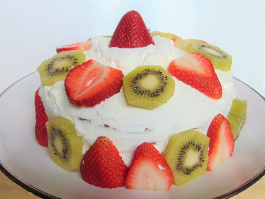 Healthy coconut flour birthday cake with whipped cream, strawberries and kiwis on white plate