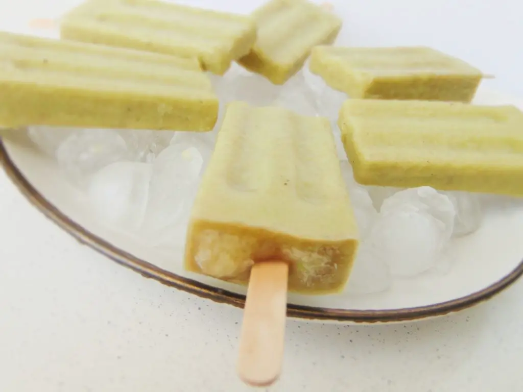 6 creamy banana and avocado popsicles laying on ice