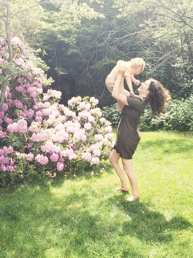 Woman holding toddler in a garden setting with pink flowers