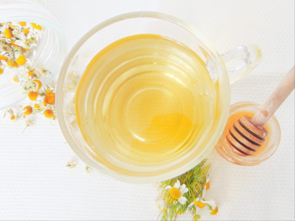 How to use chamomile flowers: chamomile tea in glass cup, chamomile flowers, honey jar, and dry chamomile flowers in background