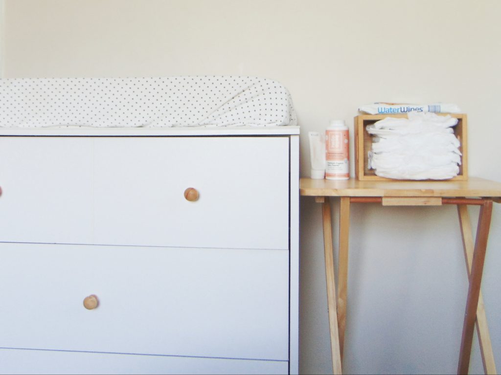 White dresser with wooden knobs and natural wood folding table used as changing station in a minimalist kid's bedroom on a budget