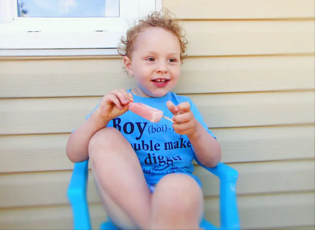 Boy eating a bone broth popsicle outdoors sitting on a blue chair