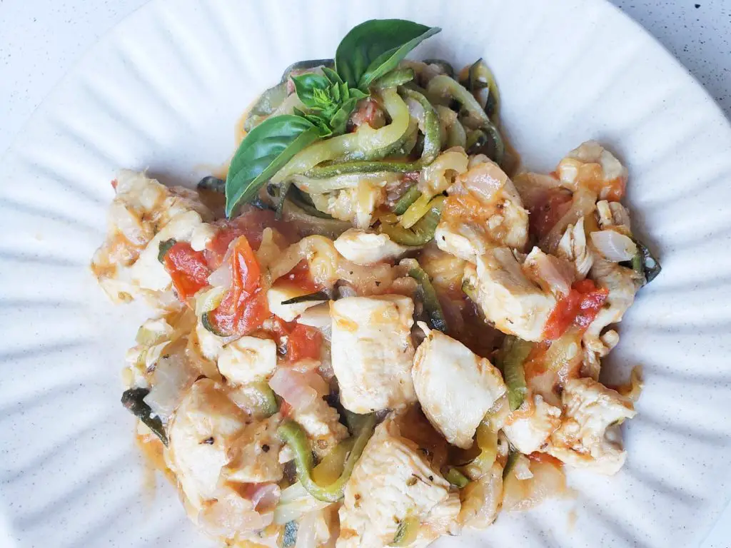 Zucchini noodles with chicken, tomatoes and parmesan cheese on white plate