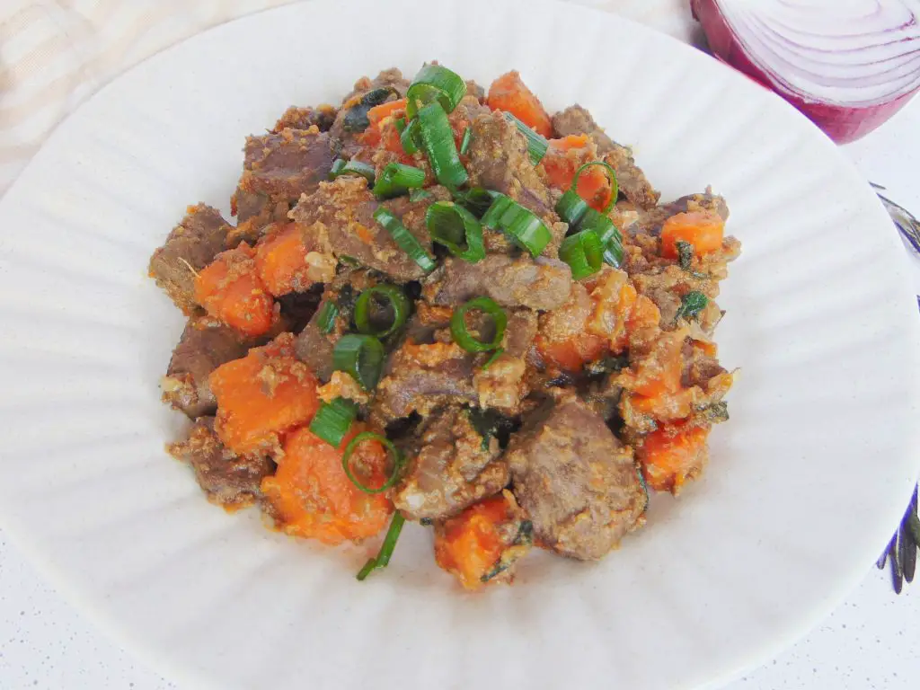 Beef liver cooked with sweet potatoes and onions and served with fresh green onions on white plate