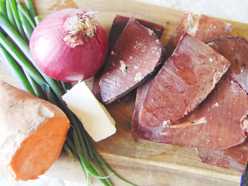 Raw beef liver slices, red onion, sweet potato, green onion and butter on wooden cutting board