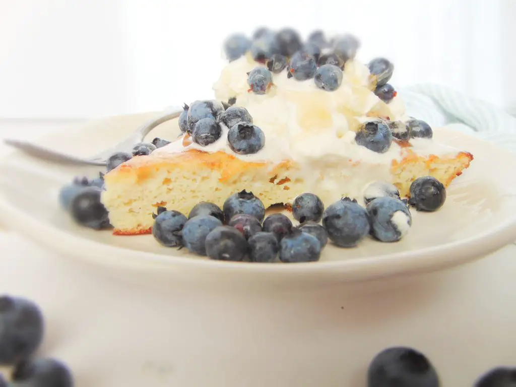 coconut flour dutch baby pancake slice garnished with whipped cream, honey, and fresh blueberries