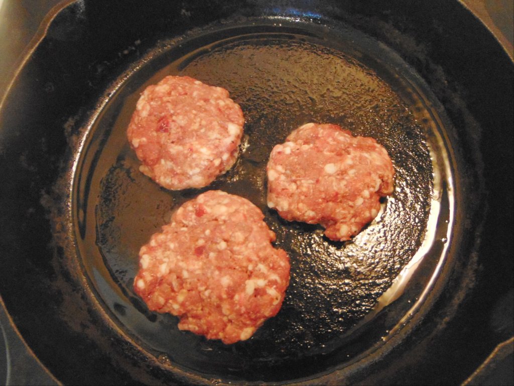 cooking organ meat sausage patties on a cast iron skillet