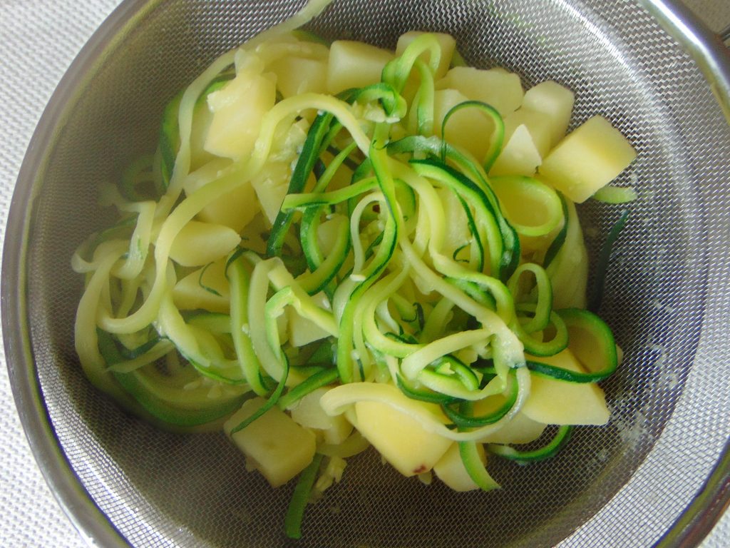 Boiled zucchini noodles and potatoes draining on colander