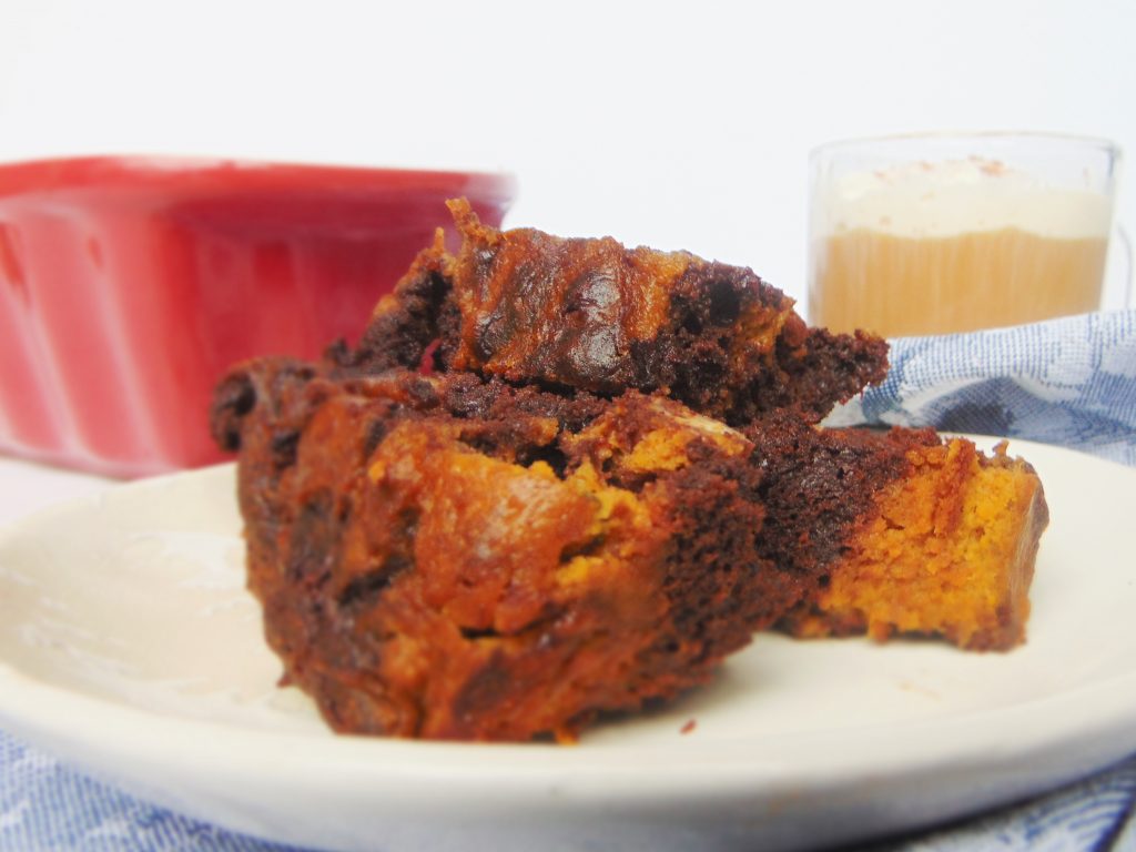 Pumpkin Swirled Chocolate Loaf Cake slices on a white plate with red loaf pan and cup of coffee in background