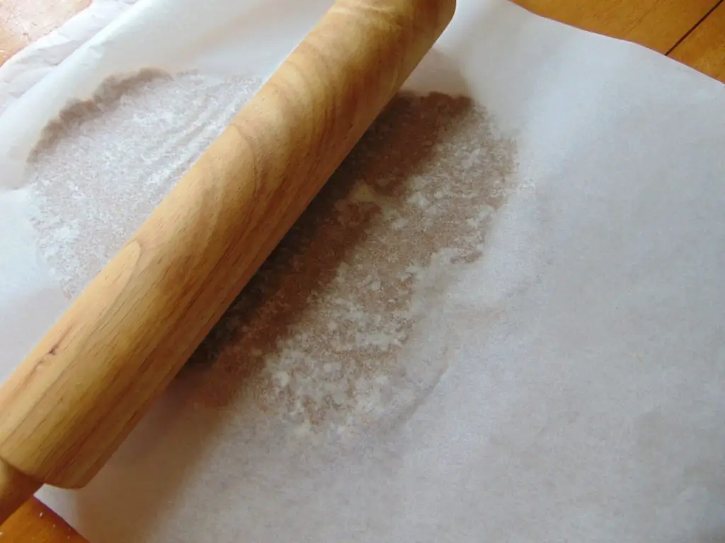 Coconut flour gingerbread man cookie dough in between parchment paper ready to be rolled