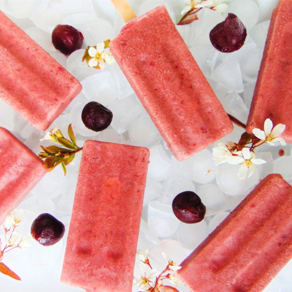 Cherry Yogurt Popsicles laying on ice with cherries and white flowers as garnish