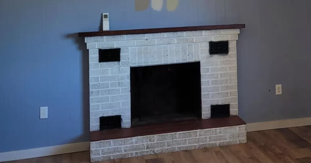 old brick fireplace painted white with red ceramic tiles and blue wall in background