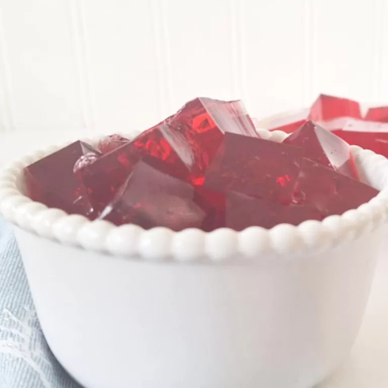 Red berry jello cubes in small white bowl made with beef gelatin