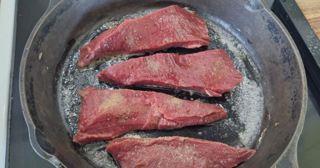 Slices of beef heart seasoned with salt, pepper and sage in hot cast iron skillet with butter being cooked