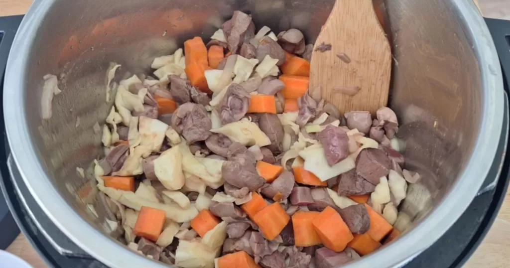 All ingredients for beef heart and kidney stew with low-carb veggies are added into the Instant Pot and combined with a wooden spatula before slow cooking