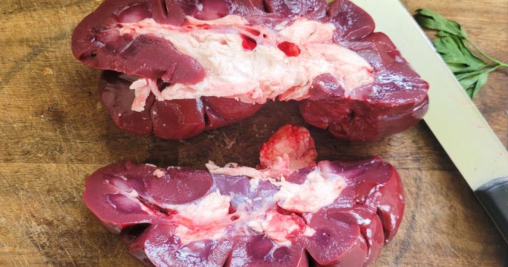 Raw beef kidney cut open in half on cutting board