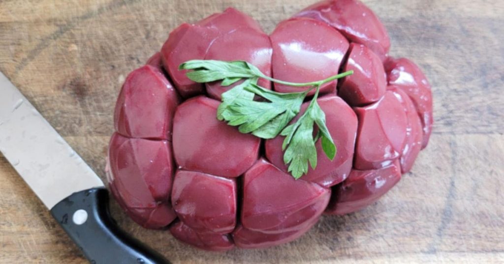 Raw whole beef kidney on cutting board with knife besides and parsley as garnish